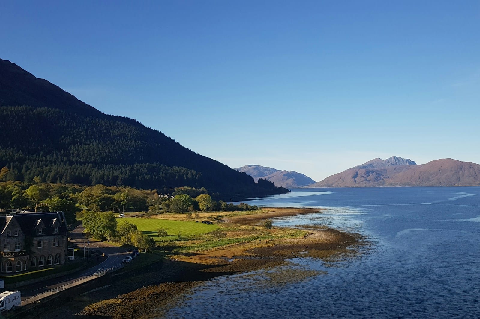 A Highland hotel on the shore of a loch under clear skies, mountains beyond